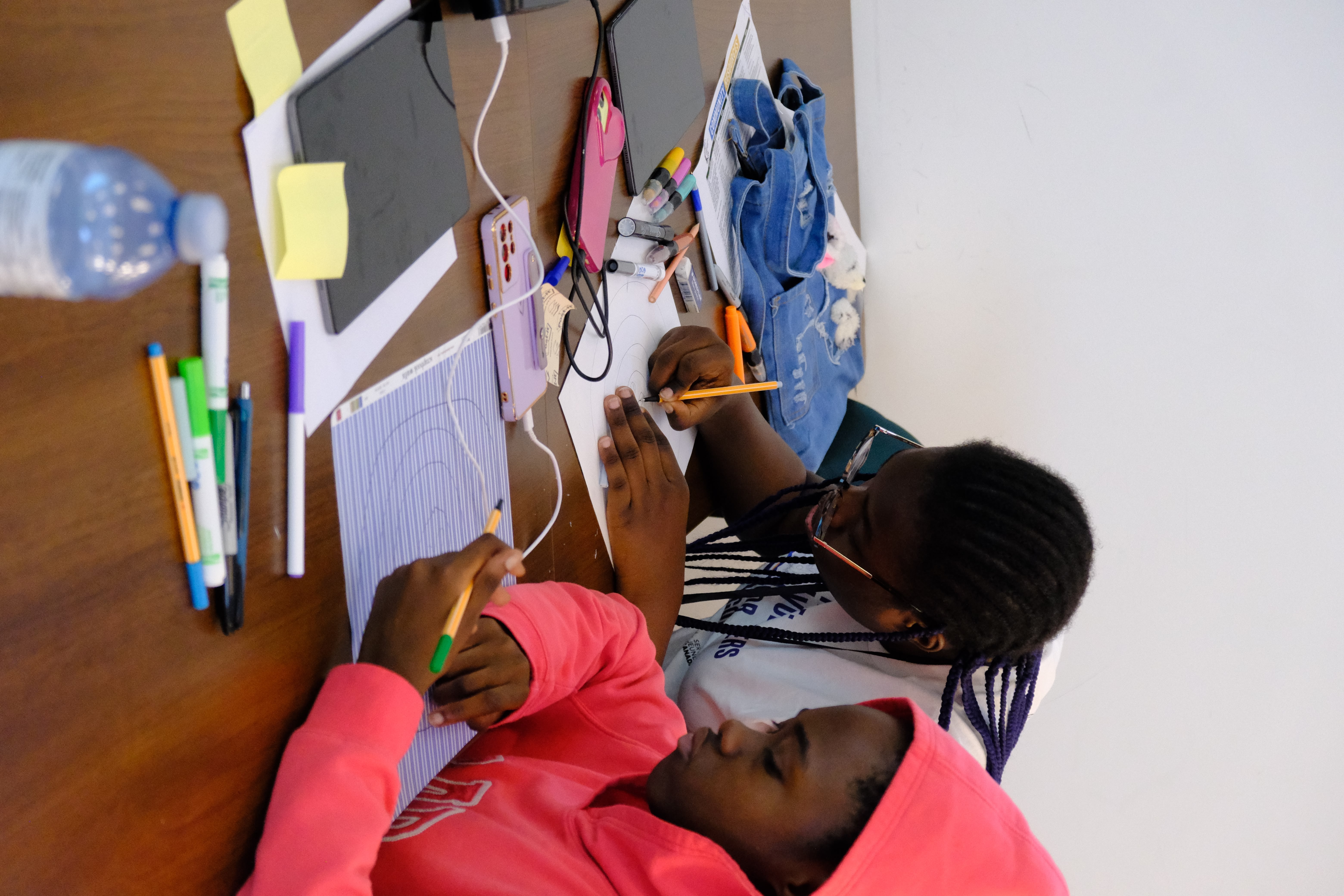 A picture of two youths colouring circles on a paper as part of the Learning How to Practice Community Workshop with Dr. Bethany Osborne on June 3, 2025