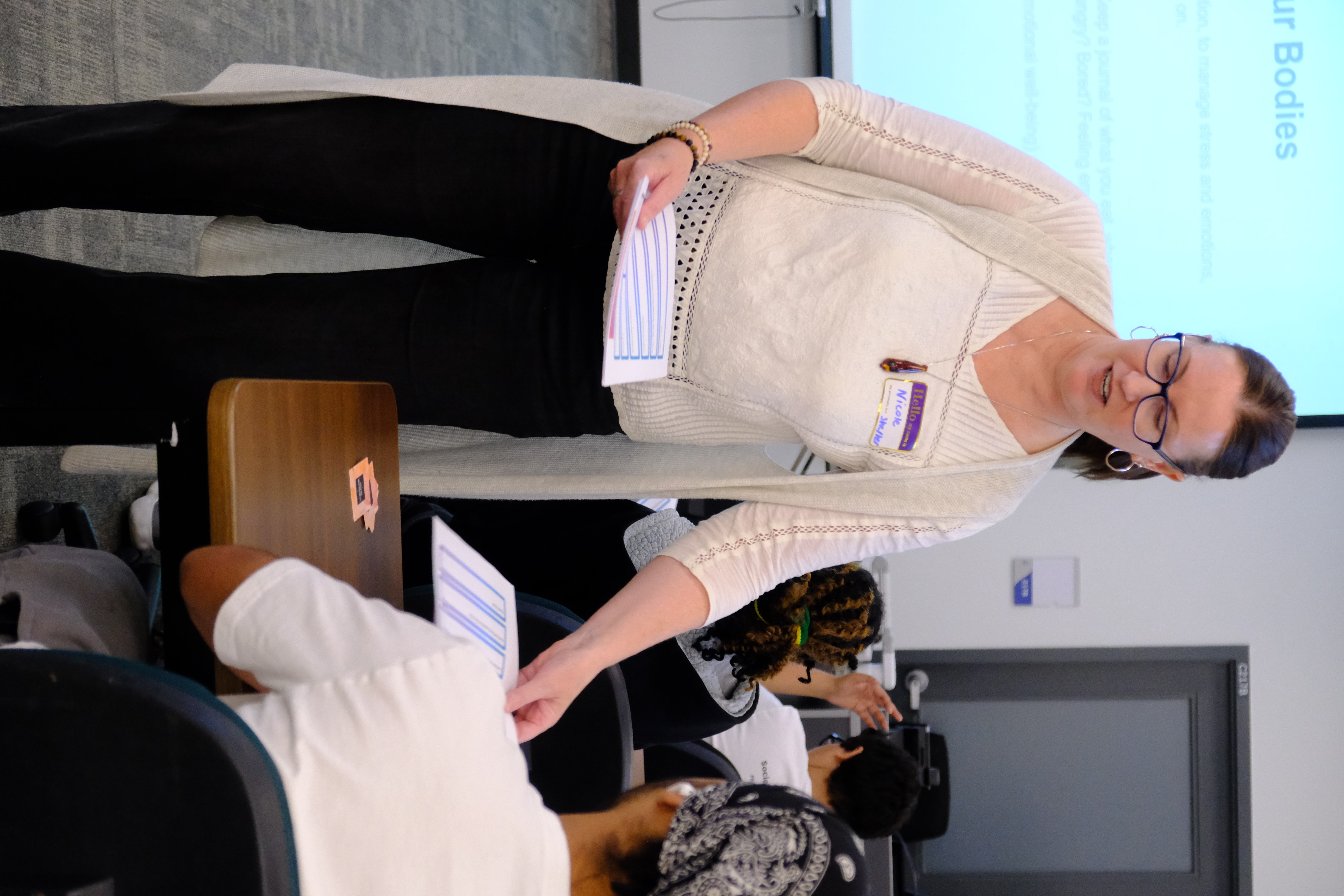 A picture of the Facilitator handing out worksheets to the youths during the Mental & Physical Wellness Workshop with Nicole Johnson on May 27, 2025