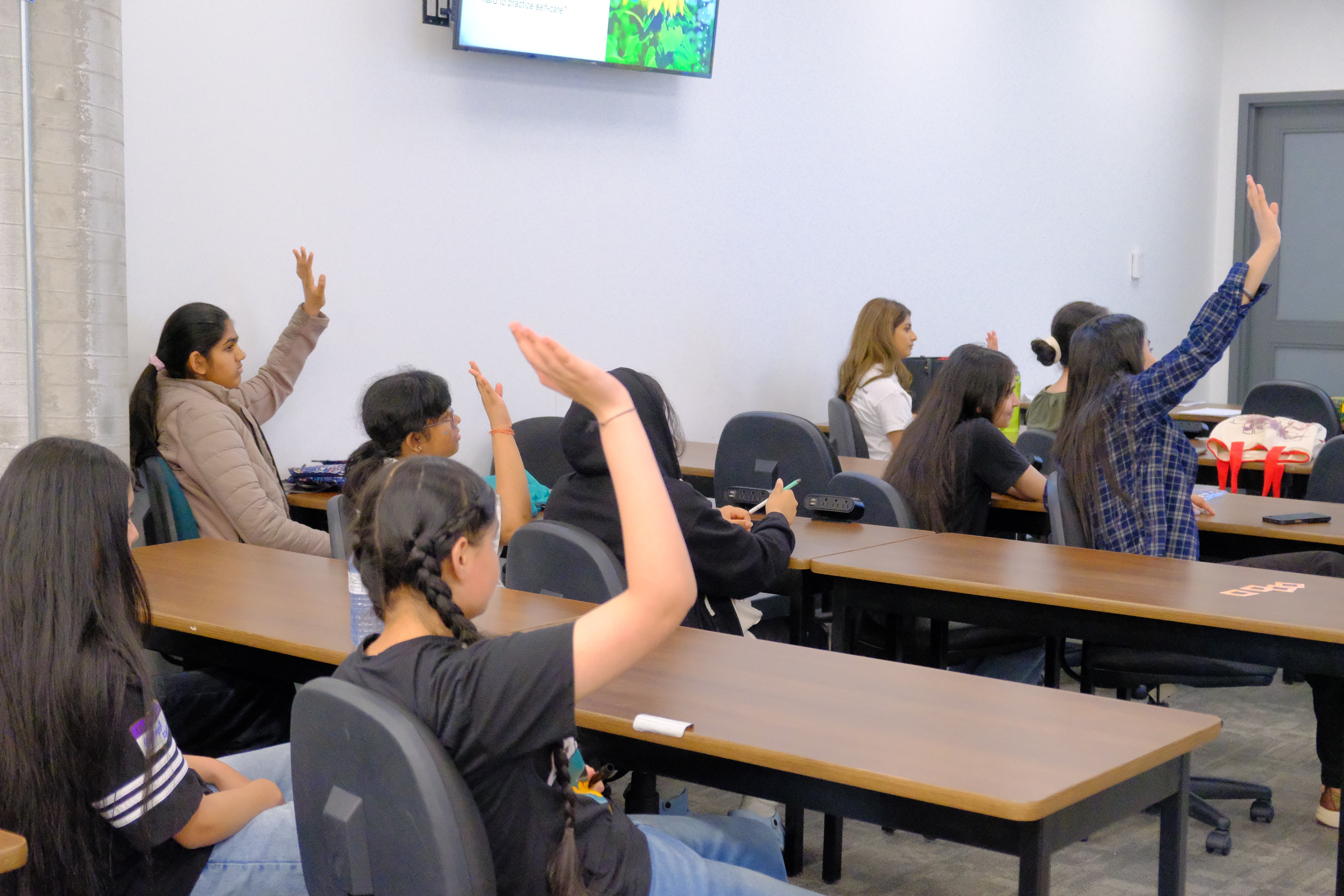 A picture of various youths raising their hands to answer questions during the Mental & Physical Wellness Workshop with Nicole Johnson on May 27, 2025