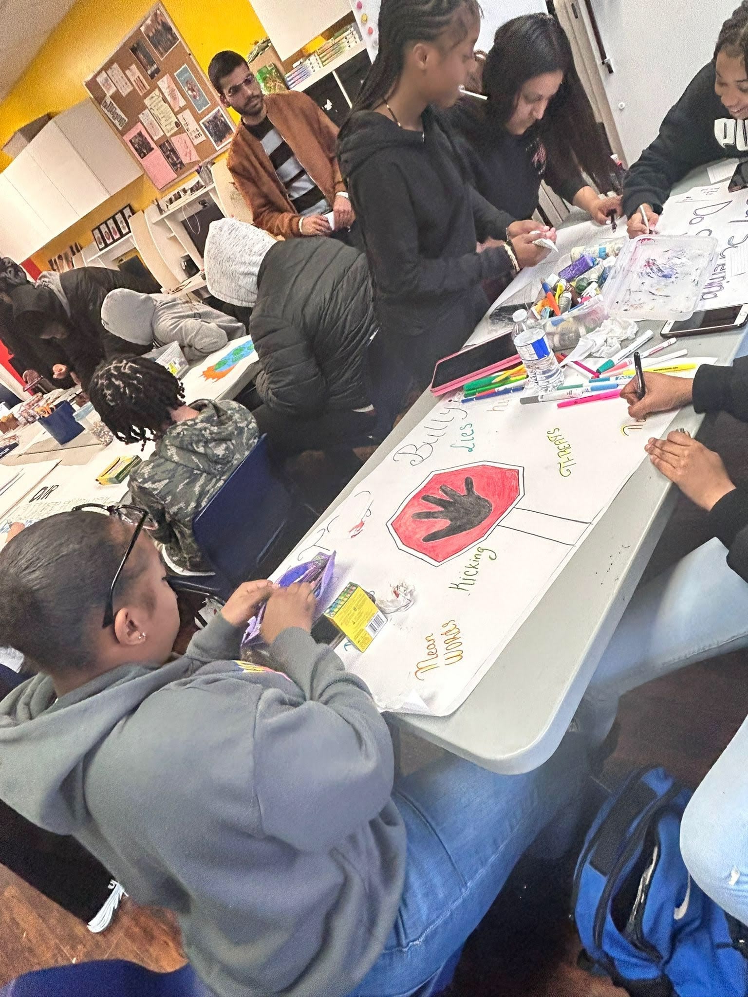 A picture of youths and a facilitator at a life skill, mental wellness and safer community workshop. The youths are creating art with a safety and anti-bullying message.