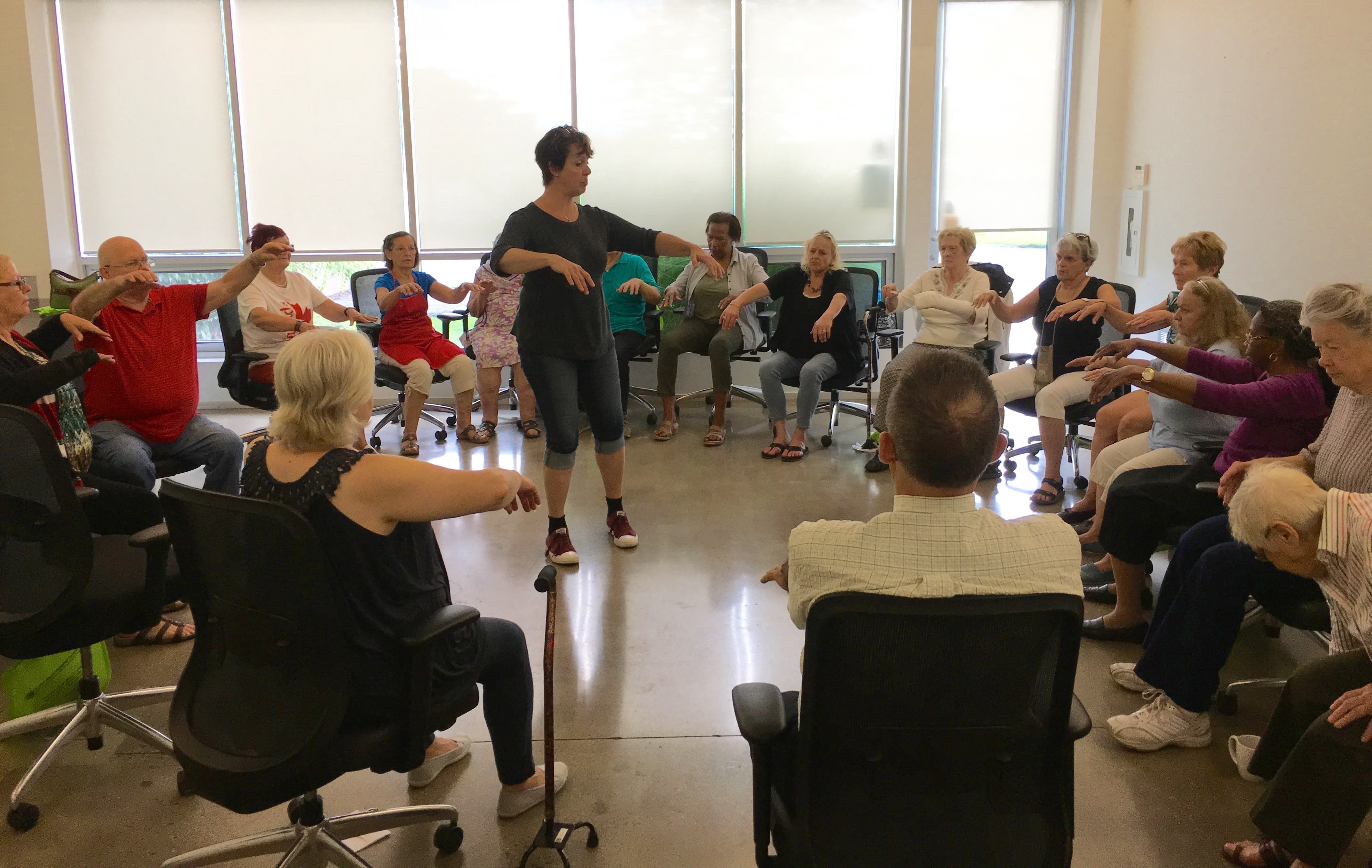 A picture of seniors and a facilitator at a theatre-based social wellness workshop. The seniors are learning a wellness exercise.